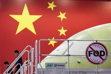 Technicians walk down a flight of stairs as a Commercial Aircraft Corp. of China Ltd. (Comac) C919 is assembled beside a large Chinese national flag hanging at the Comac Shanghai Research and Developm...