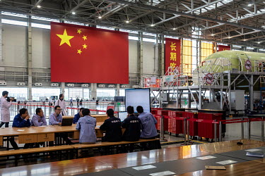 Technicians study a monitor as a Commercial Aircraft Corp. of China Ltd. (Comac) C919 is assembled beside a large Chinese national flag hanging at the Comac Shanghai Research and Development Center.