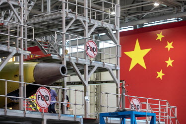 A technician walks under the tail of a Commercial Aircraft Corp. of China Ltd. (Comac) C919 aircraft as it assembled beside a large Chinese national flag hanging at the Comac Shanghai Research and Dev...