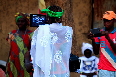 A woman films in the village square where the residents have gathered to watch a music and dance performance taking place at night and all illuminated by solar-powered lights. The villagers have paid...