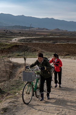 Women pushing their bicycles up a steep, unpaved road.
