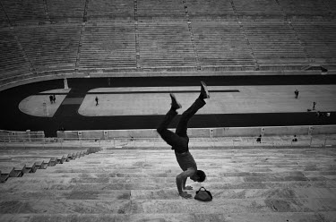 A tourist does a handstand on the seats at the old Olympic stadium.