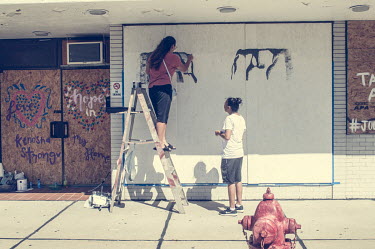 Women paint a mural on a boarded over shop front following protests, some violent, against the police shooting of Jacob Blake.