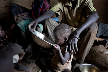 Ajany (60) feeds one of his children from a tin basin in the one room home where he lives with his brother Wol (70) and their children. Ajany's wife left about two years earlier while she was still br...