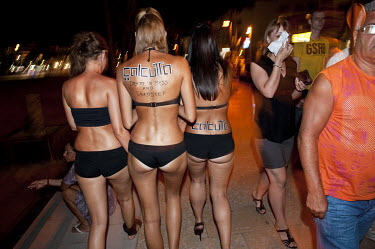 Three girls wearing black bikinis walk through the town centre to promote a party named Calcutta.