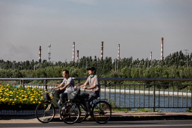 Bicyclists ride past smoke stacks rising from the city's factories and power plants.