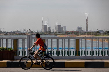 A bicyclist rides over a bridge, past smoke stacks rising from the city's factories and power plants.