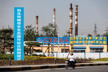 A woman rises a motor scooter past smoke stacks rising from the city's factories and power plants.