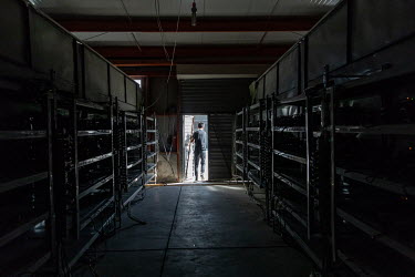 A technician walks past racks of computers at a bitcoin mining facility operated by Bitmain Technologies Ltd. Bitmain is one of the leading producers of Bitcoin-mining equipment and also runs Antpool,...
