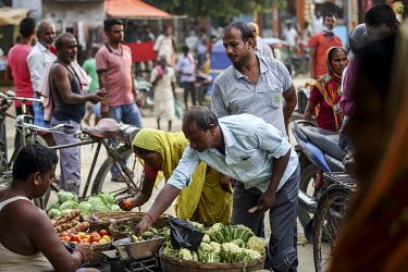 Customers inspect vegetables being sold at a roadside market stall.