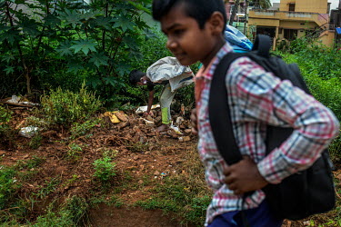 A schoolboy passes Rahul (11) as he searches through rubble while collecting plastic to sell to recyclerson the outskirts of the city.  Rahul was doing well at school until the coronavirus lockdown cl...