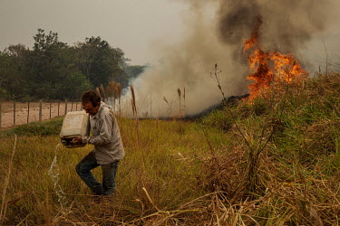 Farmer Joao Alberto Martins (53) empties a jerry can of water onto the grassy banks of a road that crosses his farm as he desperately tries to prevent a wildfire burning his property in Santo Antonio...