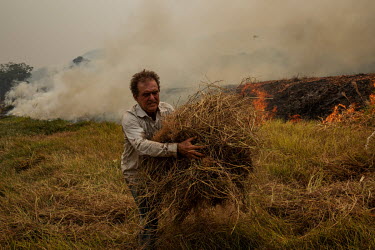 Farmer Joao Alberto Martins (53) removes combustible dry grass from the banks of a road that crosses his farm as he desperately tries to prevent a wildfire burning his property in Santo Antonio Leverg...
