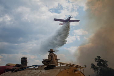 Fire fighters from the Sesc Porto Cercado hotel's private force sit on top of a water tanker looking up as an aeroplane as it drops a load of water onto a fire burning near the hotel in the Pantanal....