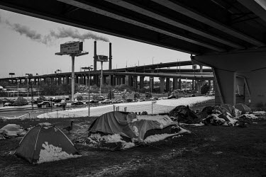 Snow partially covers tents in a homeless person's camp established under a viaduct.