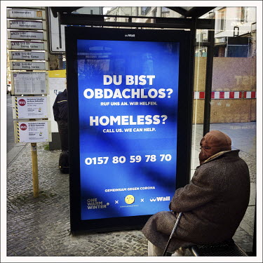A homeless person sits in front of a bus shelter advertising poster that reads 'Du Bist Obdachlos? Homeless?' On the Kurfuerstendamm.  The Berliner Ku'damm is lined with luxury boutiques, hotels and r...