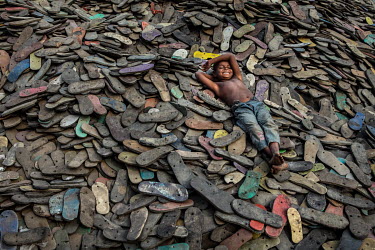 A street child lies on a huge mound of flip-flop soles at a recyclers.  It is estimated that there are more than 600,000 street children living in Bangladesh, 75% of them live in the nation's capital,...