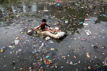 A street boy floats in a rubbish-strewn pool using a sack full of polystyrene as a raft to as he collects plastic bottles to sell to recyclers.  It is estimated that there are more than 600,000 street...