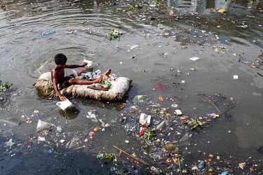 A street boy floats in a rubbish-strewn pool using a sack full of polystyrene as a raft to as he collects plastic bottles to sell to recyclers.  It is estimated that there are more than 600,000 street...