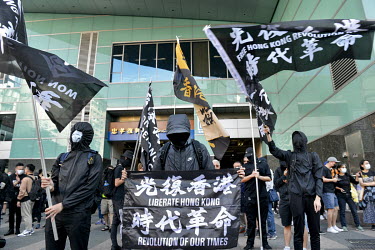 Protestors in black wave a flags and raise a banner with the slogan 'Liberate Hong Kong, Revolution of Our Times' as people gather at a metro station at the start of a rally in support of the 'HK 12'...