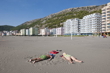 A couple lie on a sandy beach in front of new hotels along the Mediterranean coast in Shengjin.
