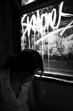 A passenger on a train sitting beside a window covered in graffiti.