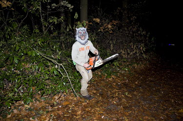 A person in werewolf mask wielding a chainsaw leaps from the undergrowth to scare people taking a night time walk on Halloween.