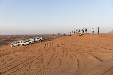 People gather on sand dunes to watch the sunset during a wheel drive desert safari.