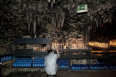 A pilgrim lights a votive candle while praying in a Lourdes grotto built in 1873 the Marquise of Courtebourne-de Nedonchel.