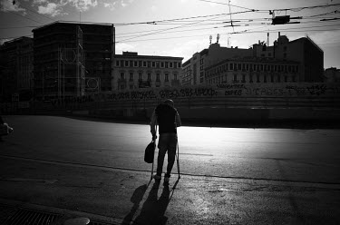 A man walking with the aid of a crutch crossing the street at Omonia Square.