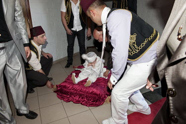 A boy of Turkish descent cries as he is carried into the hall where family and friends have gathered to celebrate his circumcision.