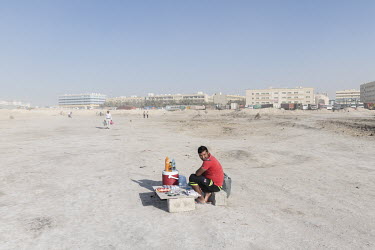 A man selling cold drinks, snacks and cigarettes from a pitch on a dusty area of waste ground near a complex of worker's labour camps at Jebel Ali.