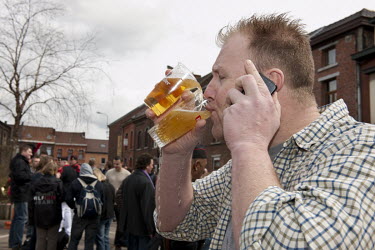 A man drinks two beers while taking a mobile phone call during the Catholic procession celebrating Saint Veronus.
