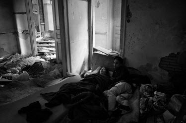 A Bangladeshi man and a disabled woman lie on an old matress inside an abandoned building.