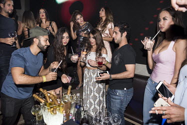 A group of men and women drink and dance at a nightclub.