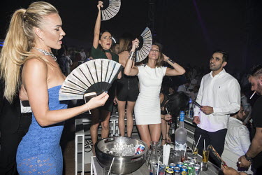 Women at a nightclub waving fans to cool down.