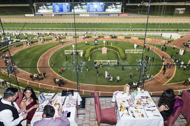 Diners at a restaurant in the Meydan Hotel, with a view over the Meydan racecourse and paddock.