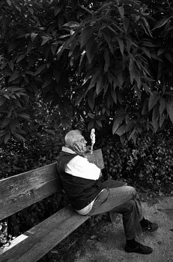An elderly man sitting on a park bench holding a Barbie doll.