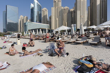 People relax on the beach at JBR, a promenade with restaurants and attractions on the Persian Gulf shoreline, flanked by the residential towers of the Dubai Marina.