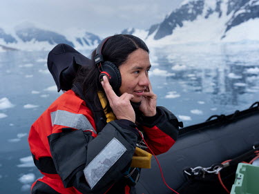 Deckhand Sam Rodriguez Camacho listens to a hydrophone picking up whale sounds in the waters off Cuverville Island in the Errera Channel.   Whales and dolphins make unique sounds whilst feeding and so...