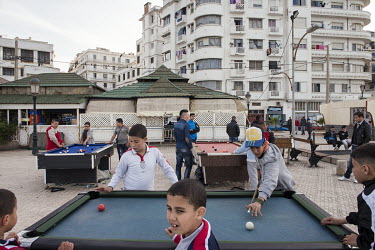 Youths play pool on an open-air tables.