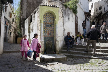 Two girls dressed in pinkl pass an old drinking fountain, decorated with tiles, in the casbah.