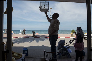 A man hangs a bird in a cage at the entrance of his shop on Rezgui Rachid Beach.