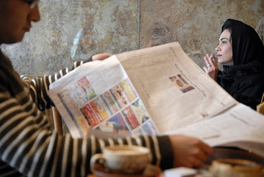 A man reading a newspaper and drinking coffee while a woman smokes a cigarette at a cafe in the embassy area of the city.