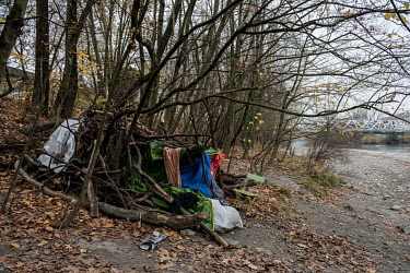 A homeless person's shelter beside the Avre River made with branches draped with old tents and sleeping bags and occupied by a teenage Morroccan boy.