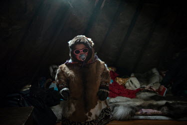 Angelina (4) standing near an entrance of a tent ('chum') wearing a yagushka, a traditional Nenets women's dress made from reindeer hide and furs.