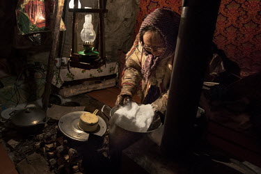 An elderly Nenets woman melting a block of snow in a pot on a stove. Snow and ice are the main sources of drinkable water for nomadic Nenets.
