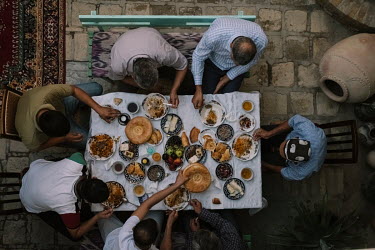 Male wedding guests, who seated together, chat over the breakfast meal of pilaf, 'lepyoshka' (local round bread), salads, pomegranate, cakes, vodka, and green tea.