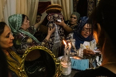 Mukhsram, a Koranic celebrant, leads loud call-and-response prayers with the bride, Ruxsora, and female wedding guests. On her way to the ceremonial curtain, Ruxora is ushered with two loaves of 'lepy...