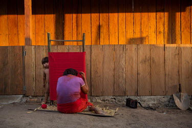 An Arawete woman in the village Paratati weaves a red skirt on a hand loom. Behind her is a wooden house built with funding from the company in charge of the Belo Monte hydropower plant.